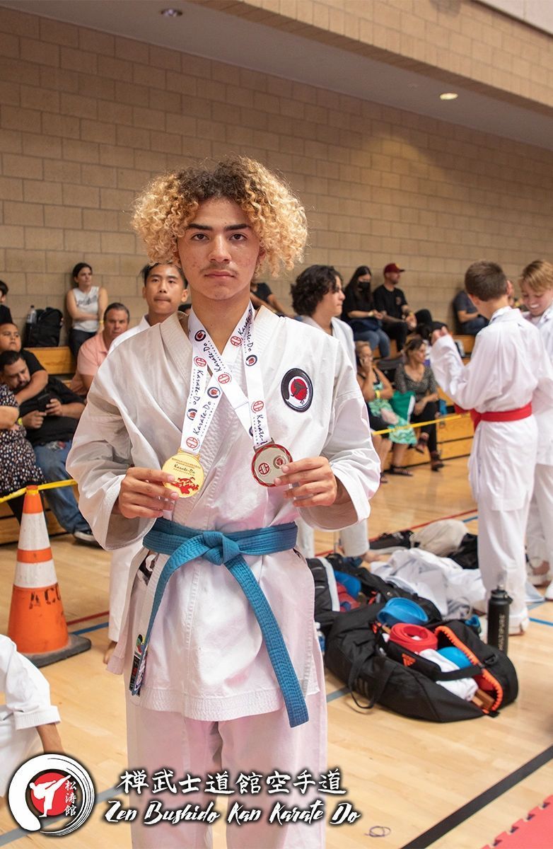 A young man in a karate uniform is holding a medal.