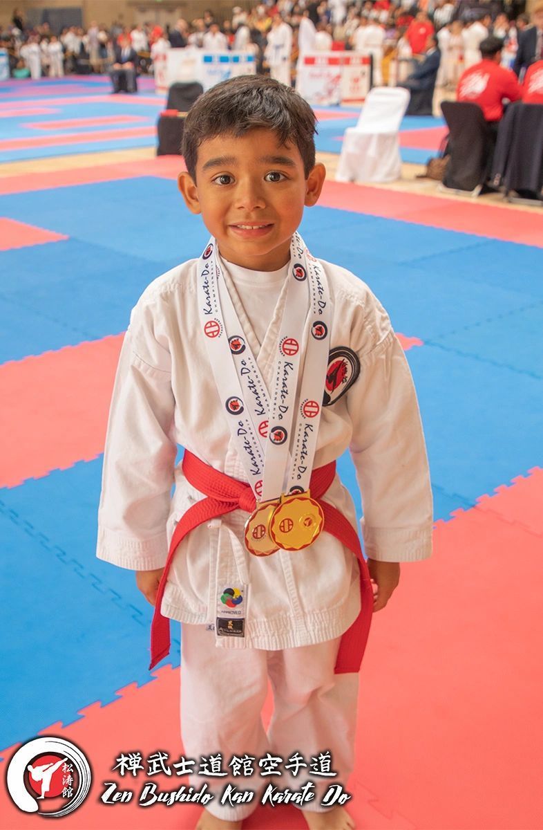 A young boy is wearing a medal around his neck while standing on a karate mat.