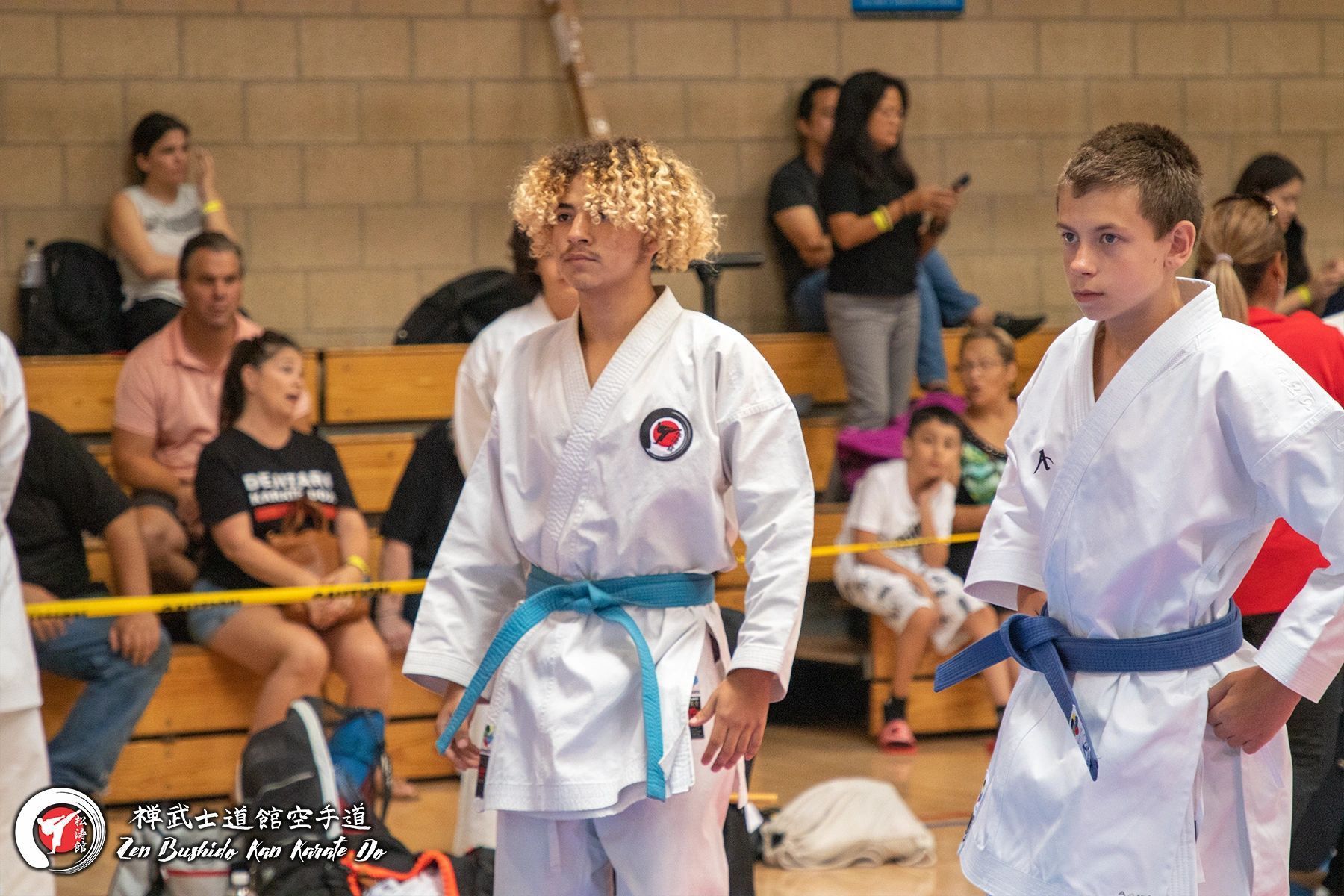 A woman in a white karate uniform with a blue belt is standing next to a boy in a white karate uniform.