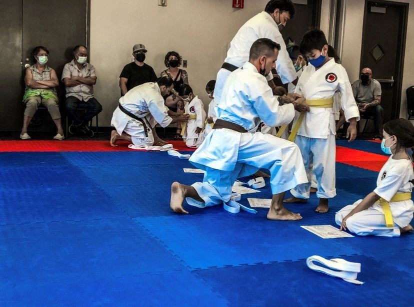 A group of people in karate uniforms are kneeling on a blue mat.