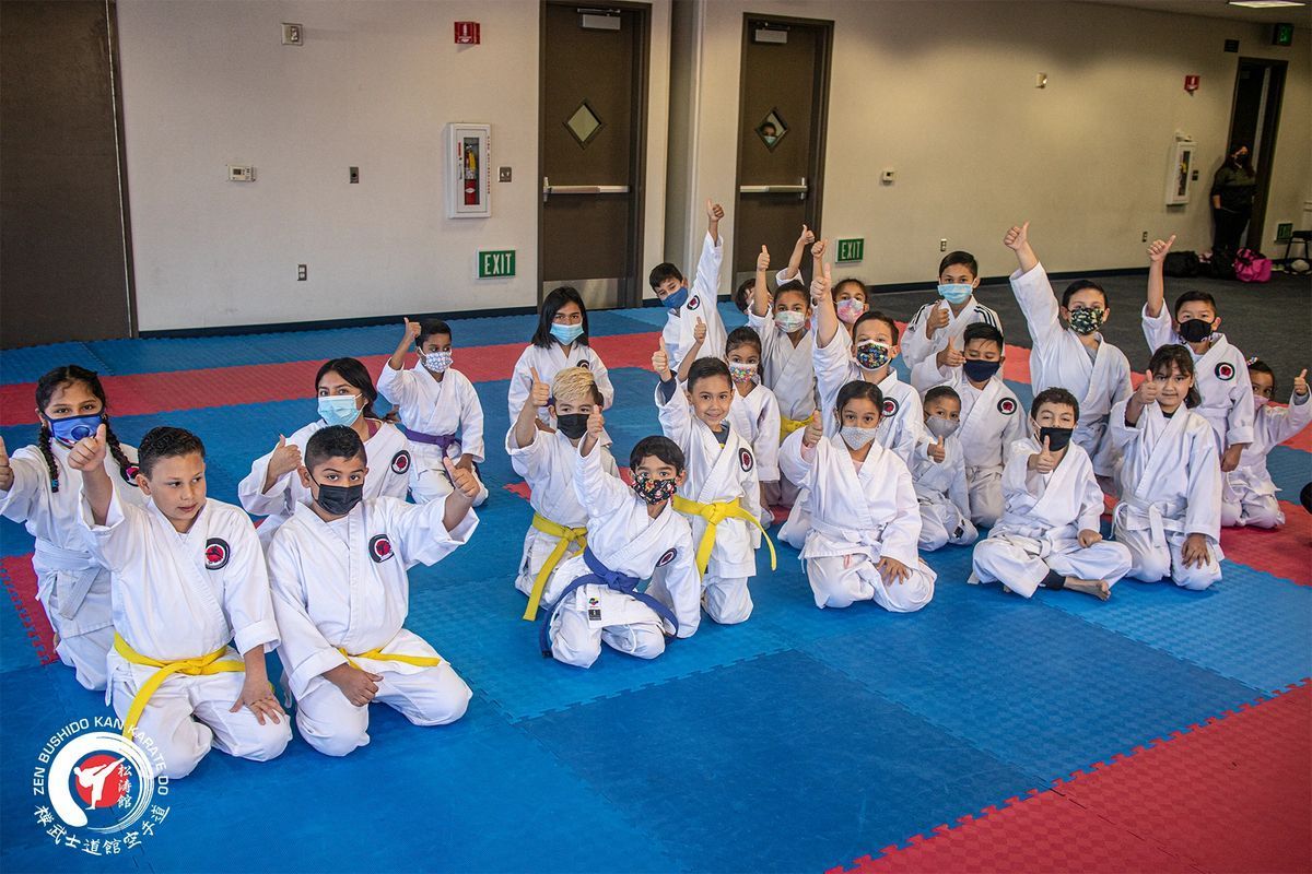 A group of children in karate uniforms are sitting on a mat in a gym.