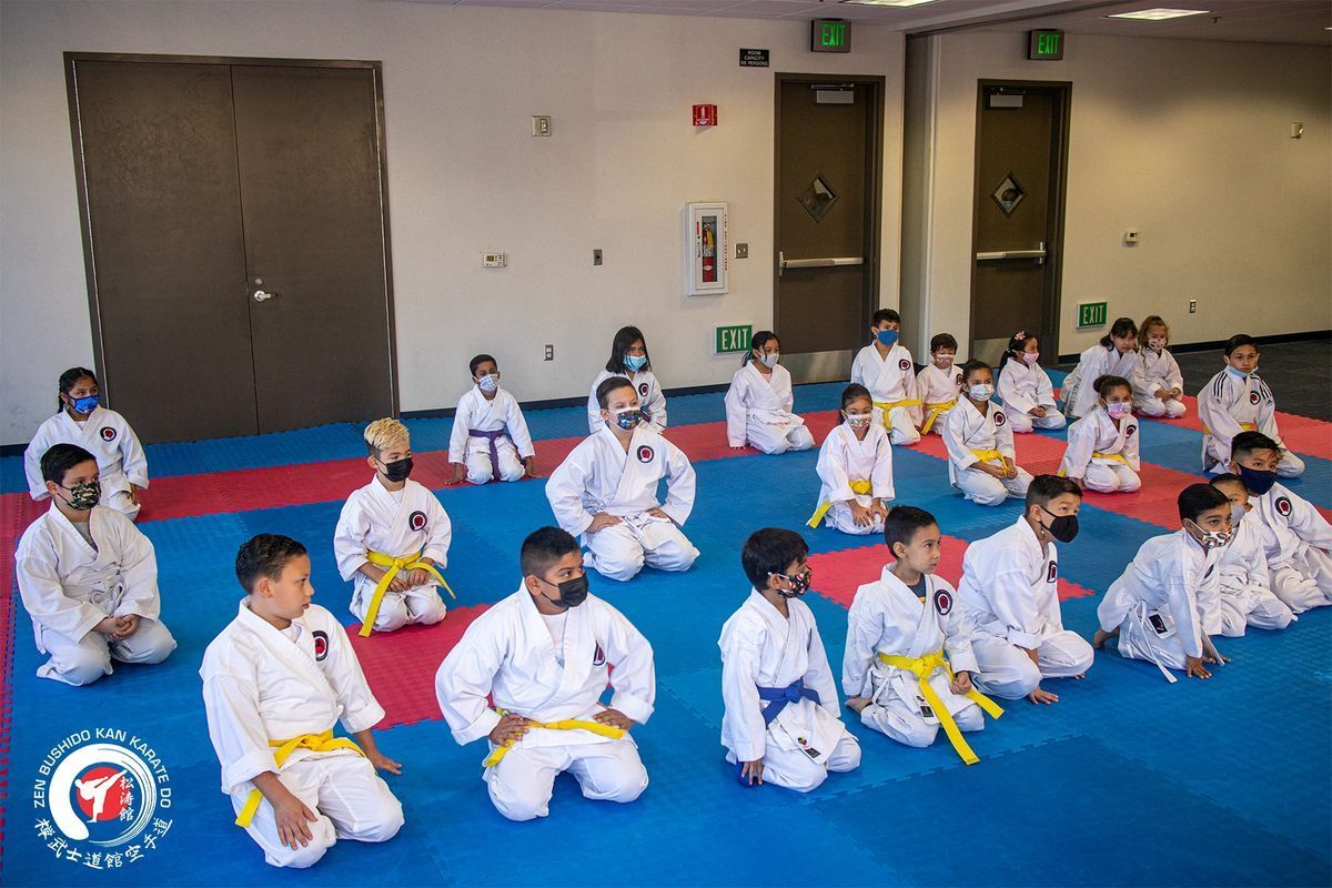 A group of children are sitting on a blue mat in a room.