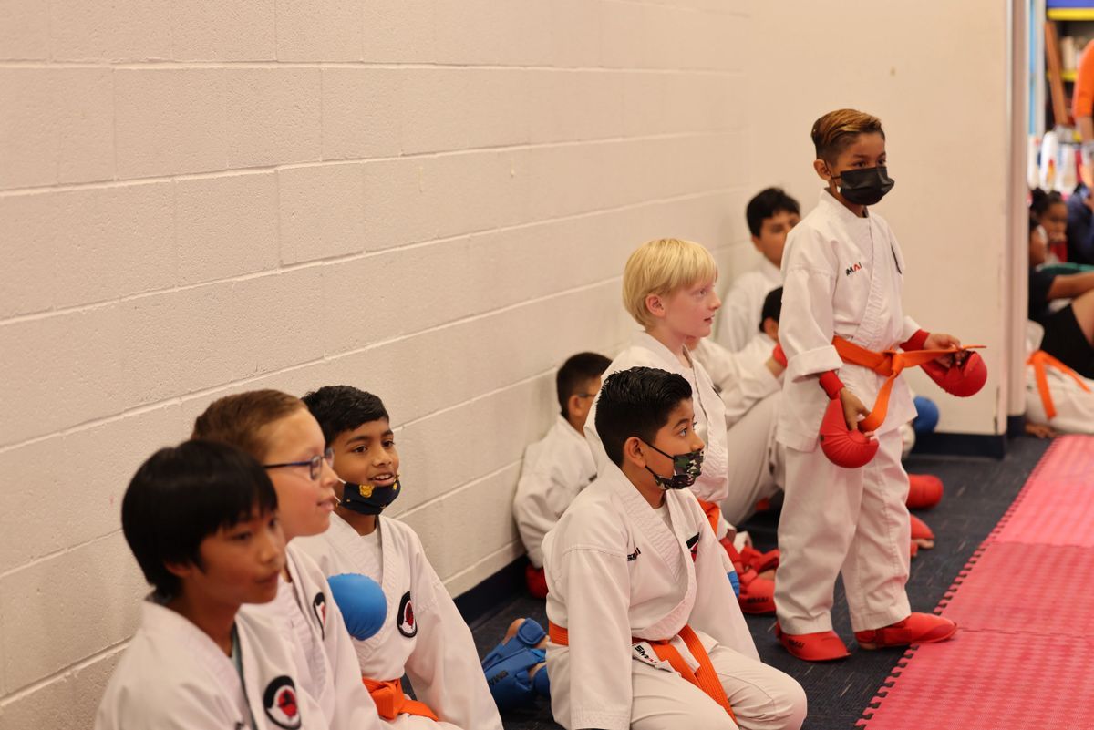 A group of young boys in karate uniforms are sitting on the floor.
