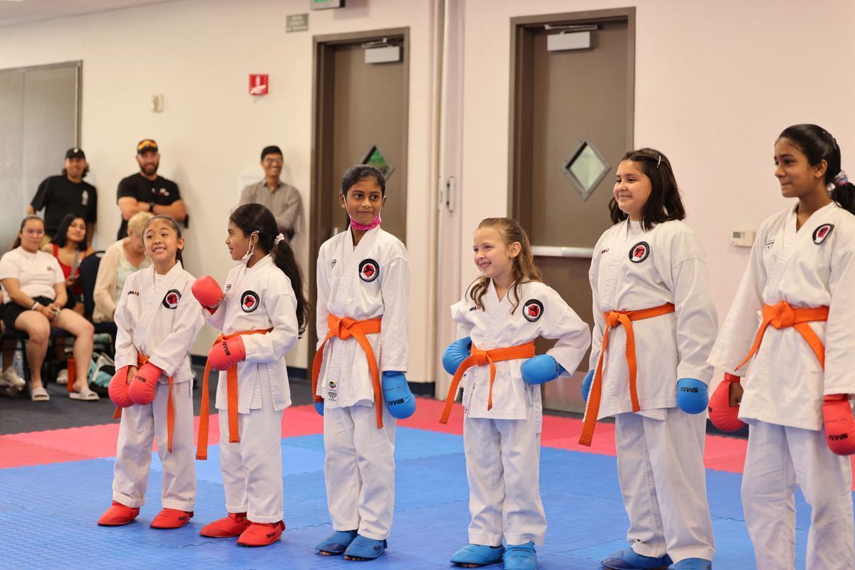 A group of young girls in karate uniforms are standing on a mat.
