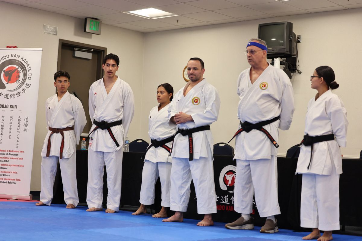 A group of people in karate uniforms are standing on a blue mat