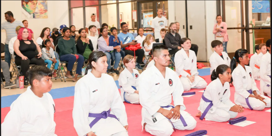 A group of people in karate uniforms are sitting on a mat.