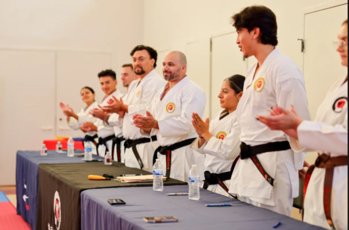 A group of people in karate uniforms are standing around a table applauding.