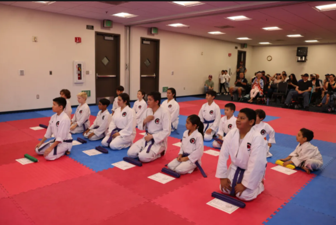 A group of kids in karate uniforms are sitting on a mat