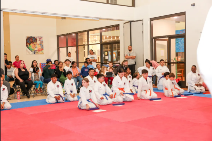 A group of people are sitting on a red mat in a gym.