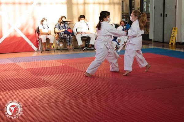 Two young girls are practicing karate on a red mat.