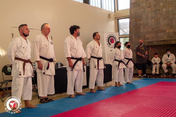 A group of men in white karate uniforms are standing on a red and blue mat.