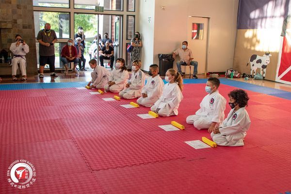 A group of people are sitting on a red mat in a gym.