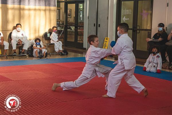 Two young boys are playing karate on a mat in a gym.