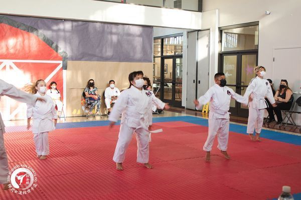 A group of children wearing masks are practicing karate on a mat.
