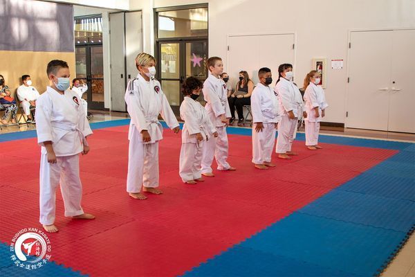 A group of children in white karate uniforms are standing on a red and blue mat.