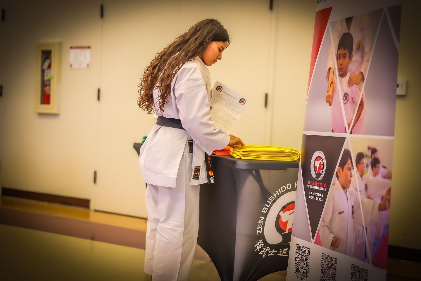 A woman in a karate uniform is standing next to a trash can.