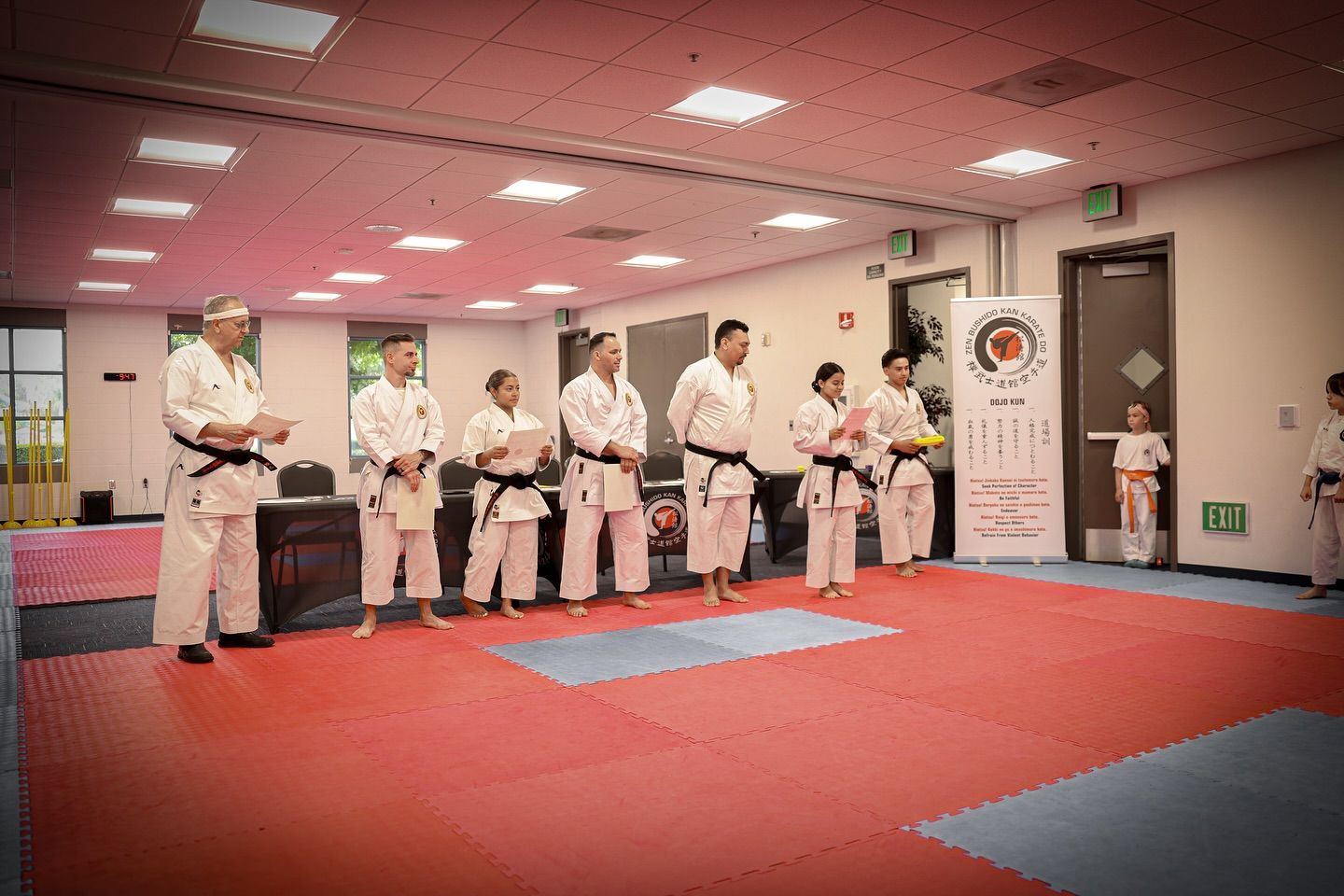 A group of people in karate uniforms are standing on a red mat in a gym.