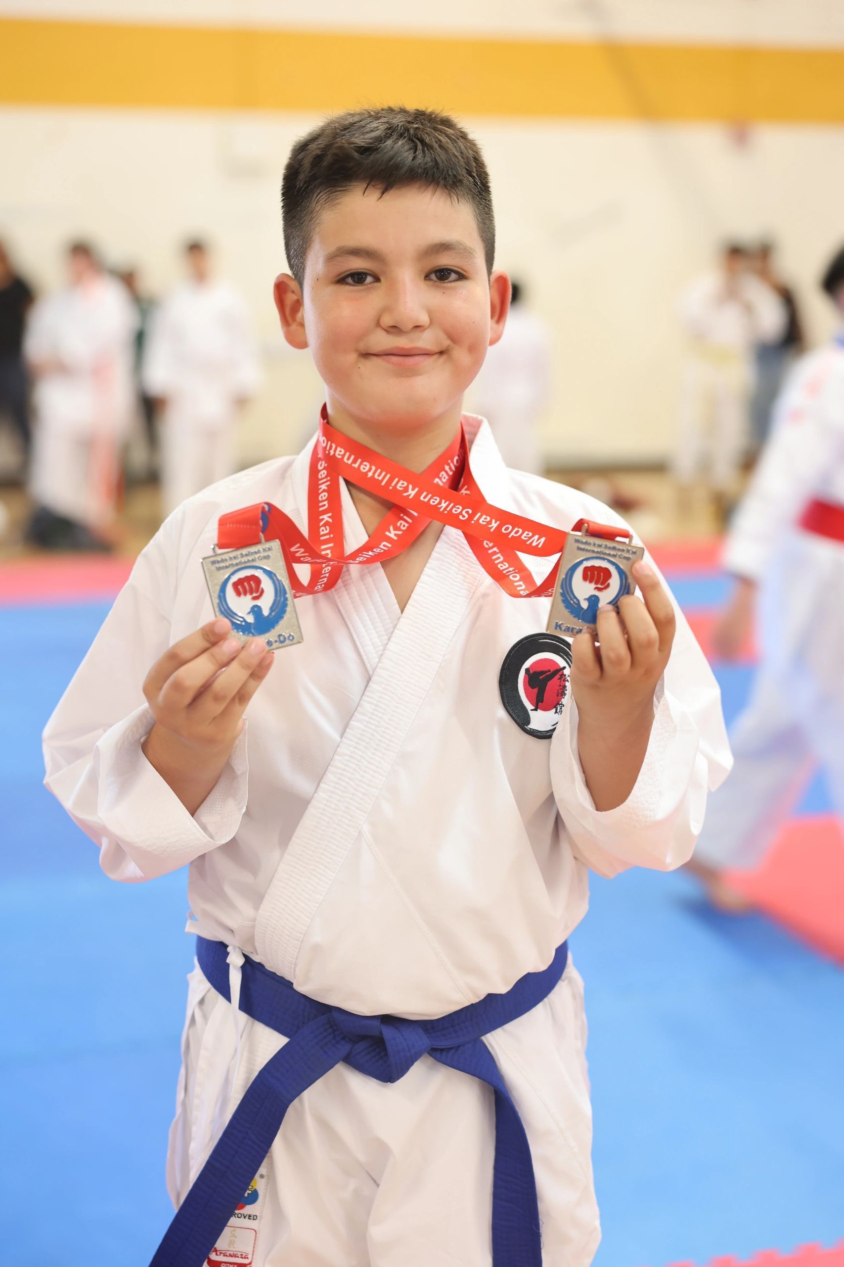 A young boy in a karate uniform is holding two medals.