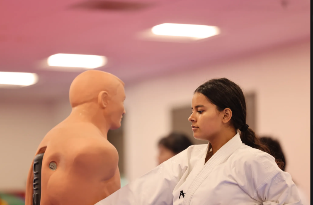 A woman in a white karate uniform is standing next to a mannequin