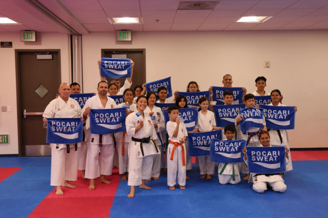 A group of people in karate uniforms are holding signs that say pocari sweat