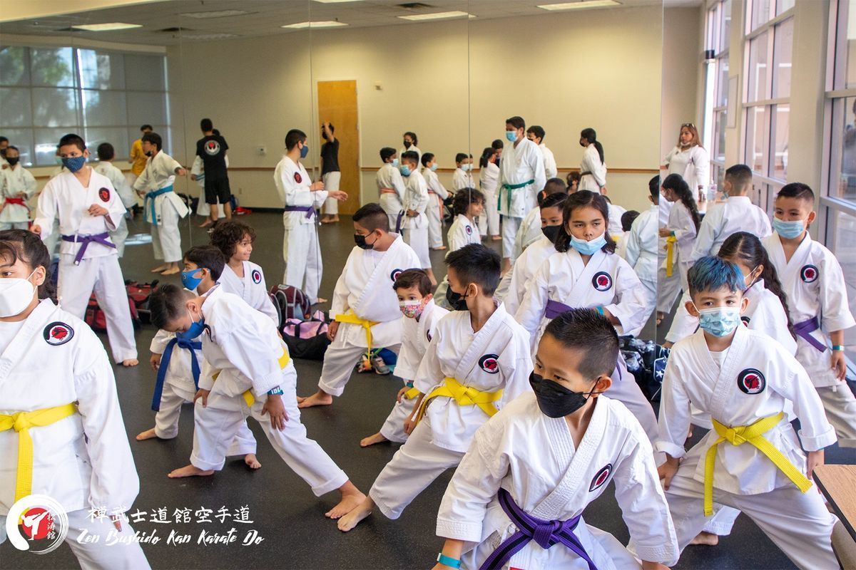 A group of children wearing masks are practicing karate in a gym.