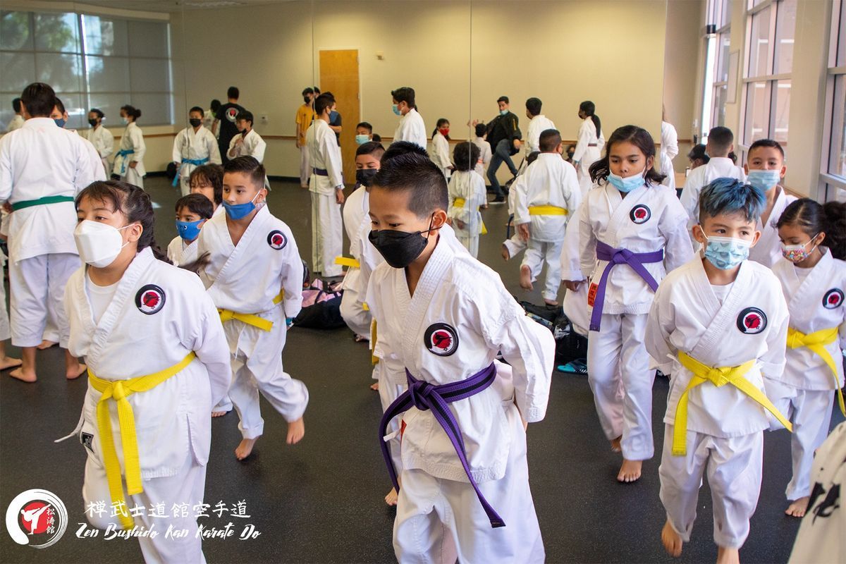 A group of children wearing karate uniforms and masks are walking in a room.