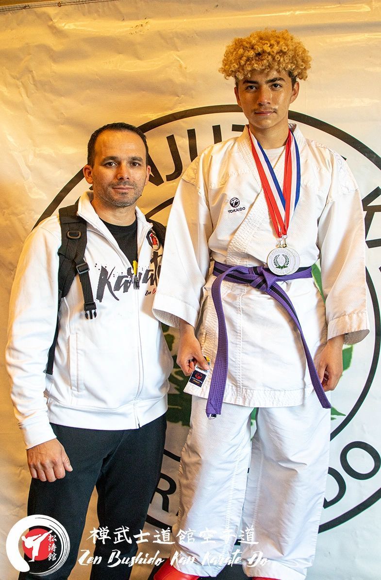 A man is standing next to a young man in a karate uniform.