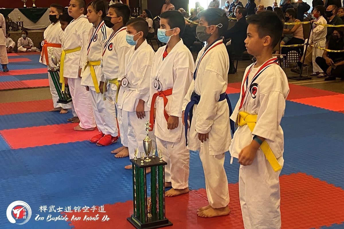A group of young boys in karate uniforms are standing next to a trophy.