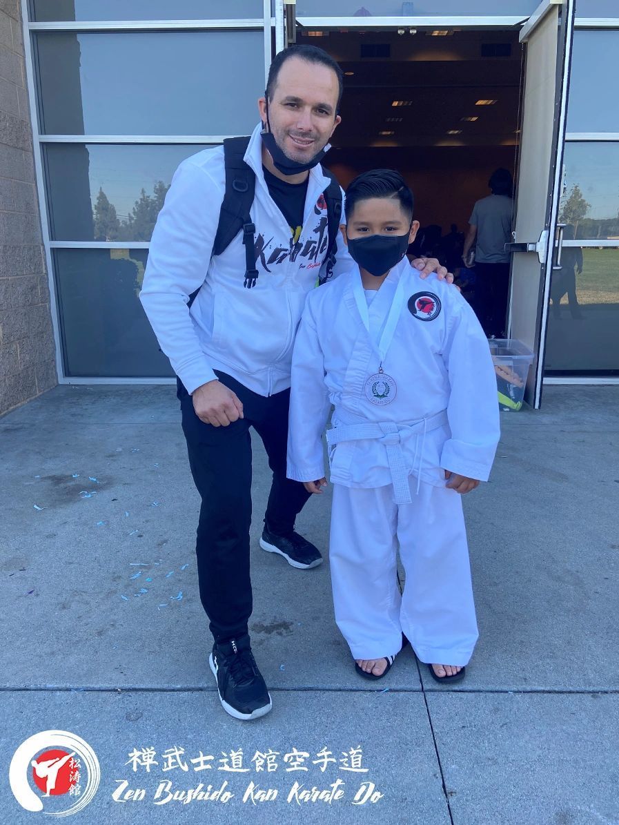A man and a boy are posing for a picture in front of a building . the boy is wearing a mask.