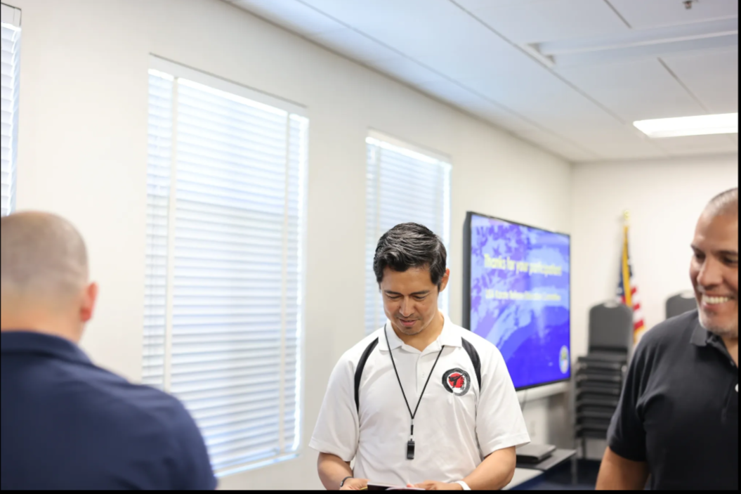 A man with a lanyard around his neck is standing in a room with other men