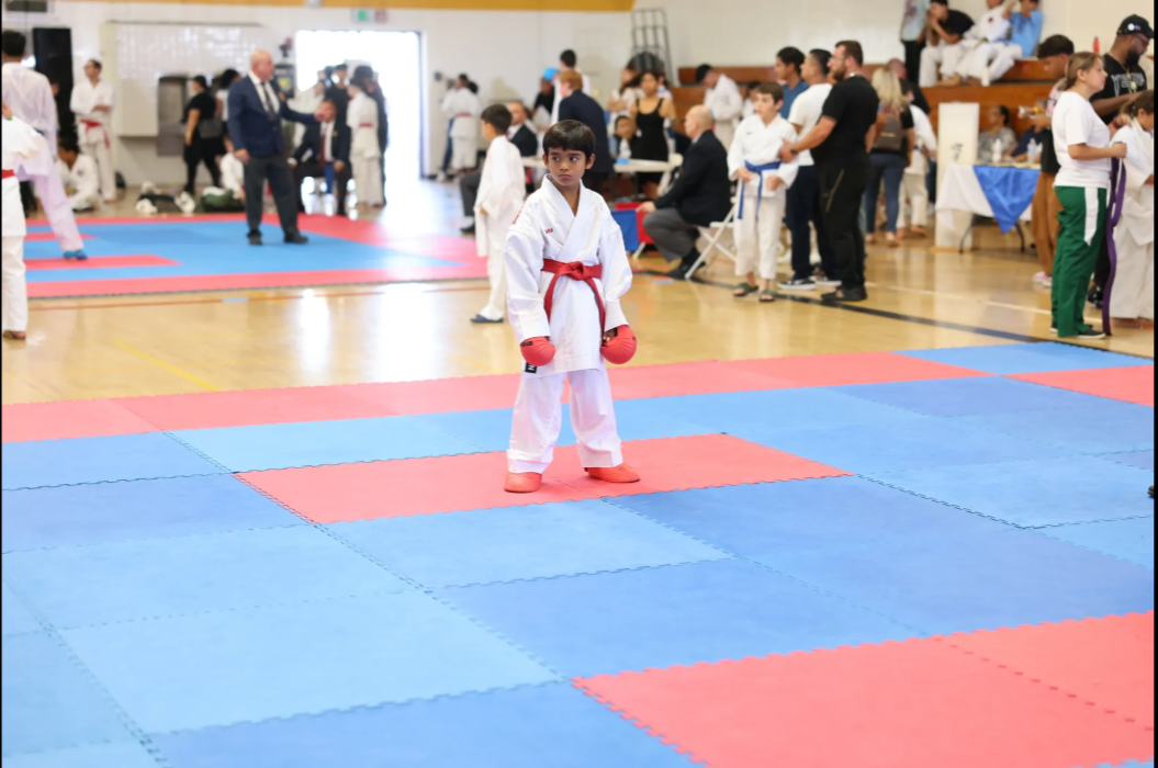 A young boy in a karate uniform is standing on a blue and red mat.