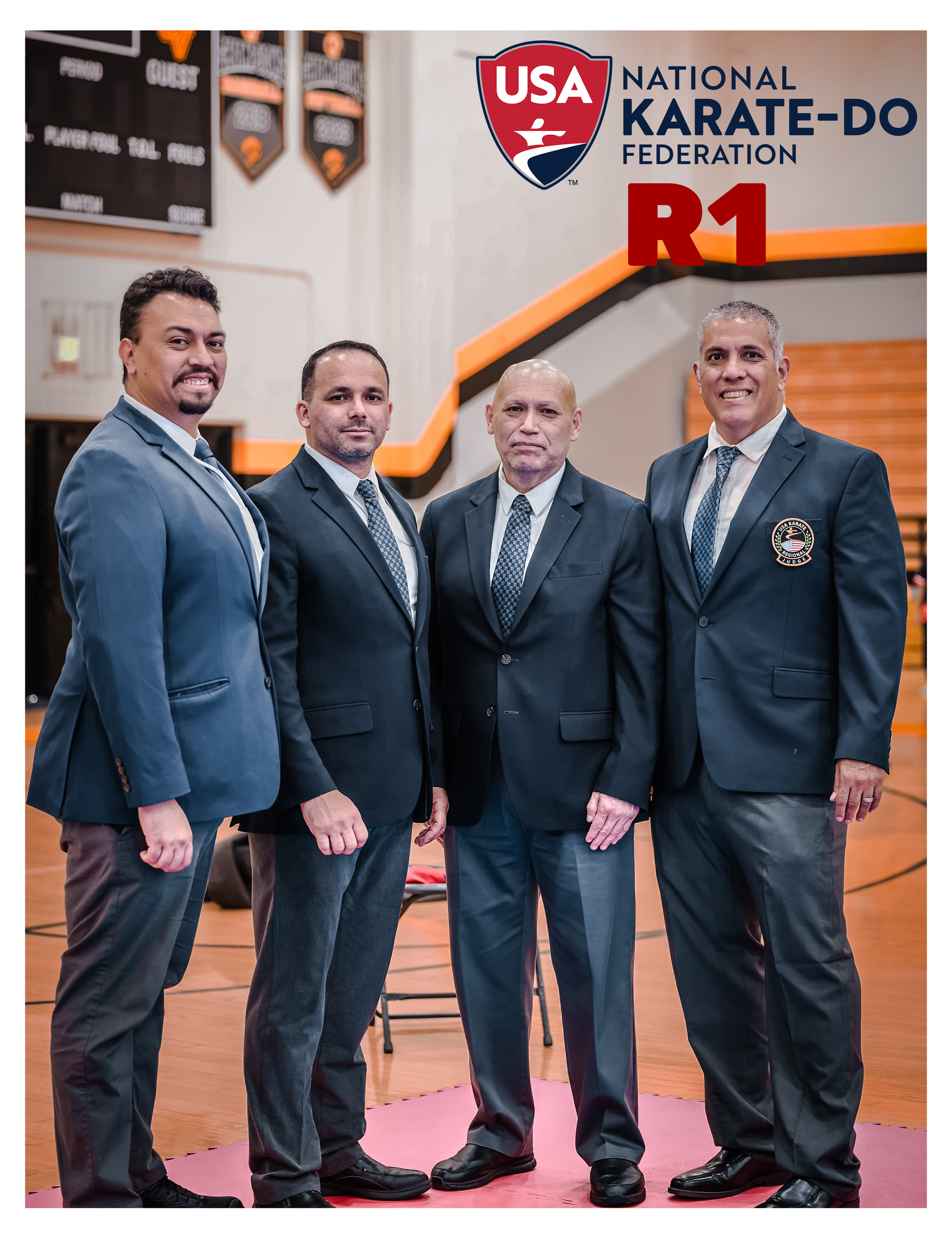 Four men in suits and ties are standing next to each other in a gym.