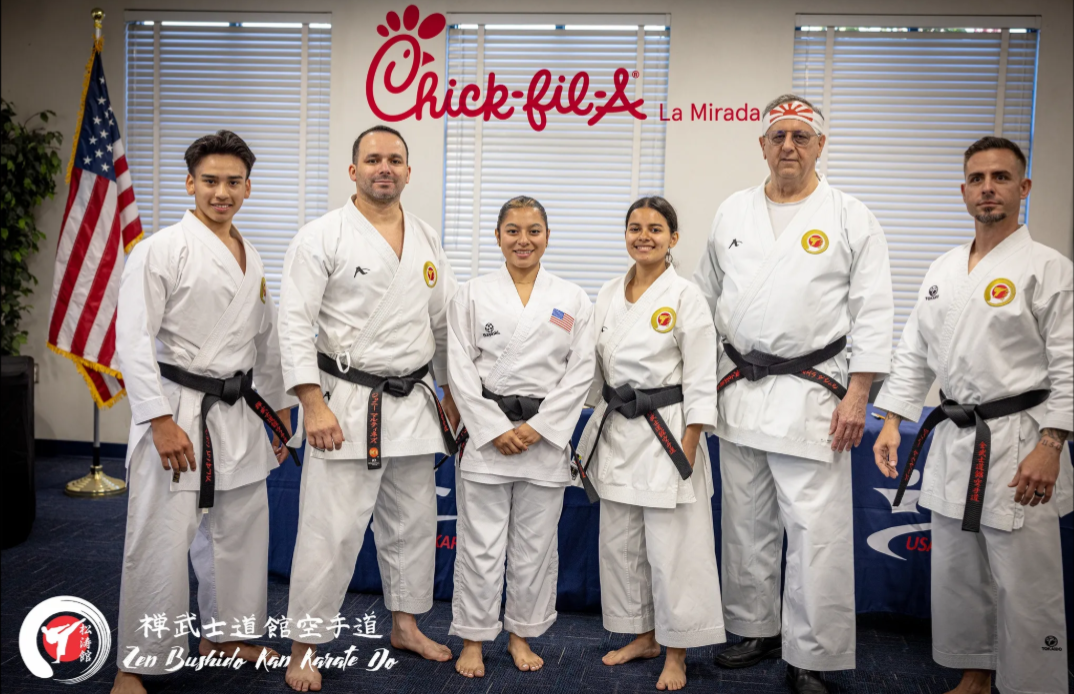 A group of people in karate uniforms are posing for a picture in front of a chick-fil-a sign.