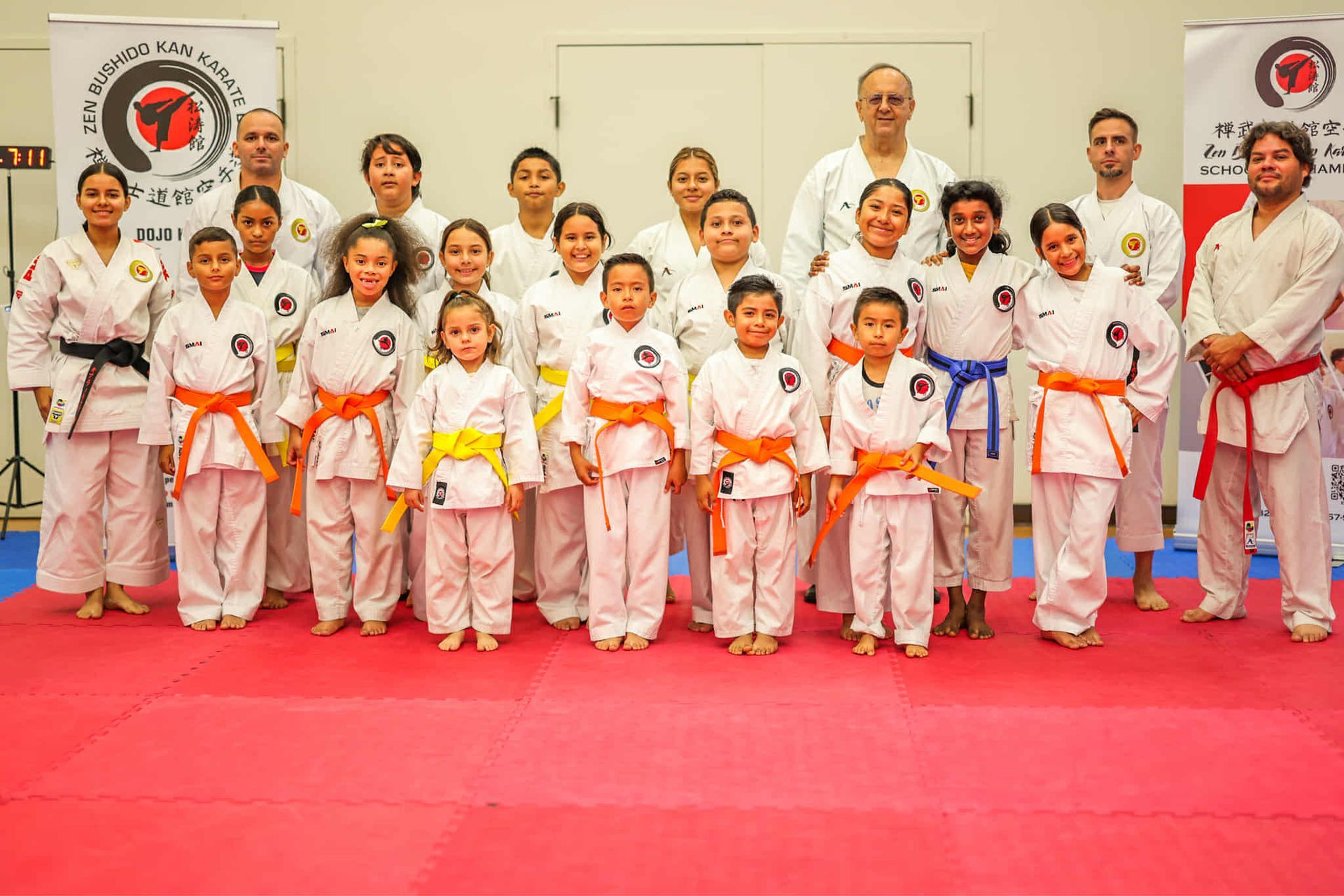 Group of karate students in white uniforms, belts of varying colors, pose together in a dojo.