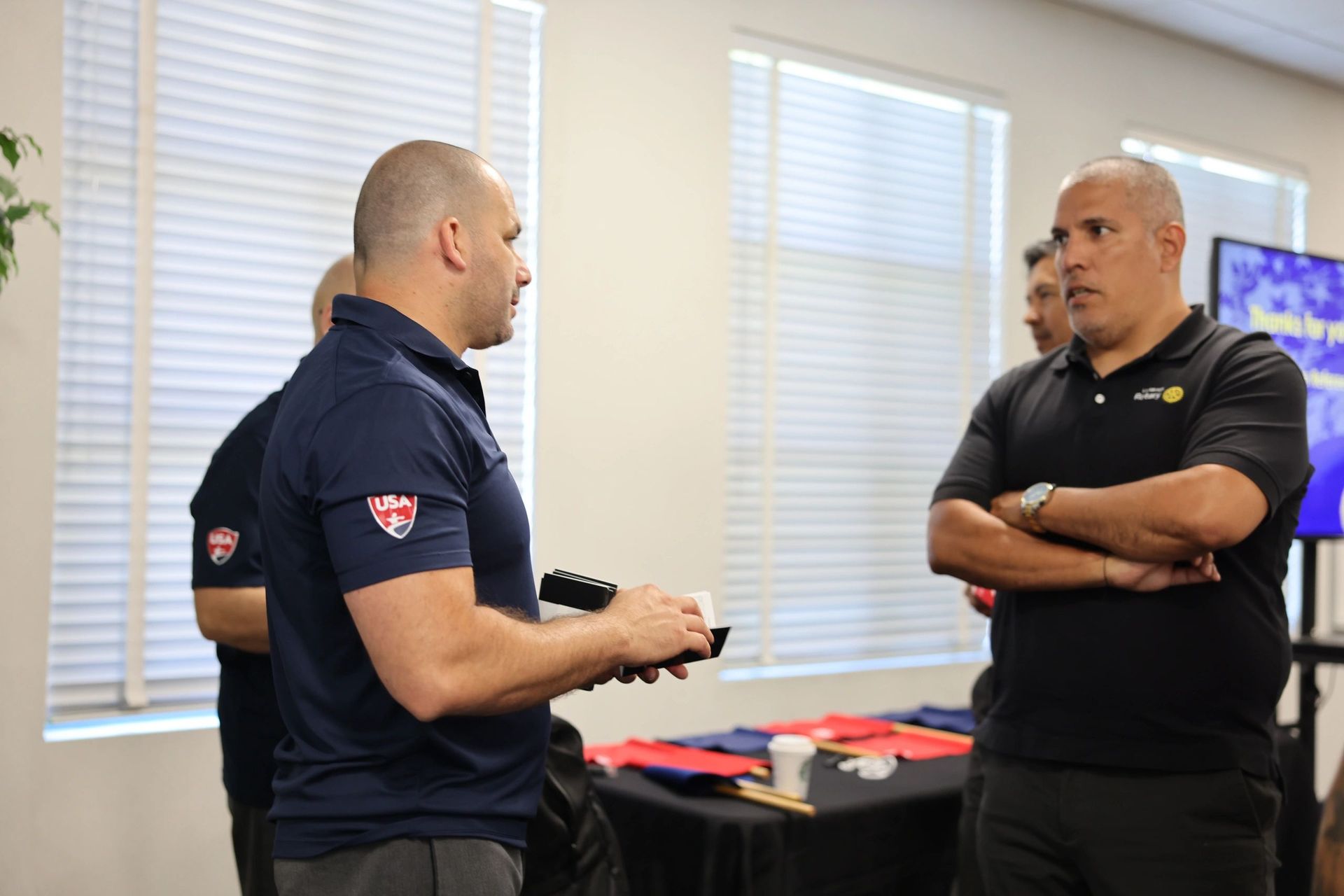 A group of men are standing in a room talking to each other.