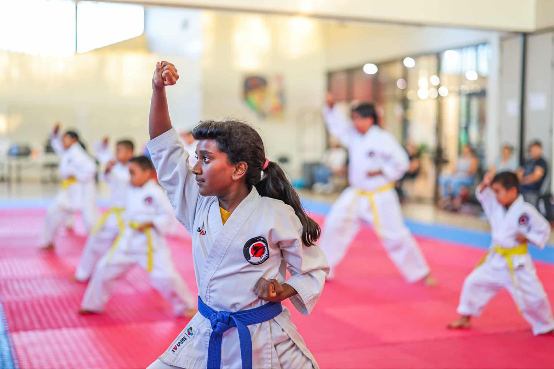 Group of children practicing karate in a dojo. A girl in blue belt is in focus, punching upwards.