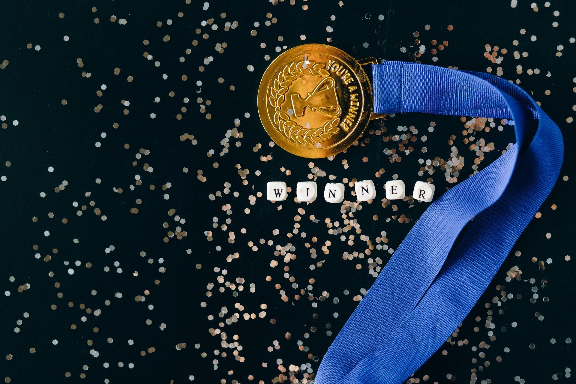 Gold medal with blue ribbon next to the word "WINNER" on a black background, with confetti.