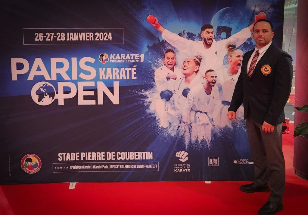 A man stands in front of a poster for the paris karate open