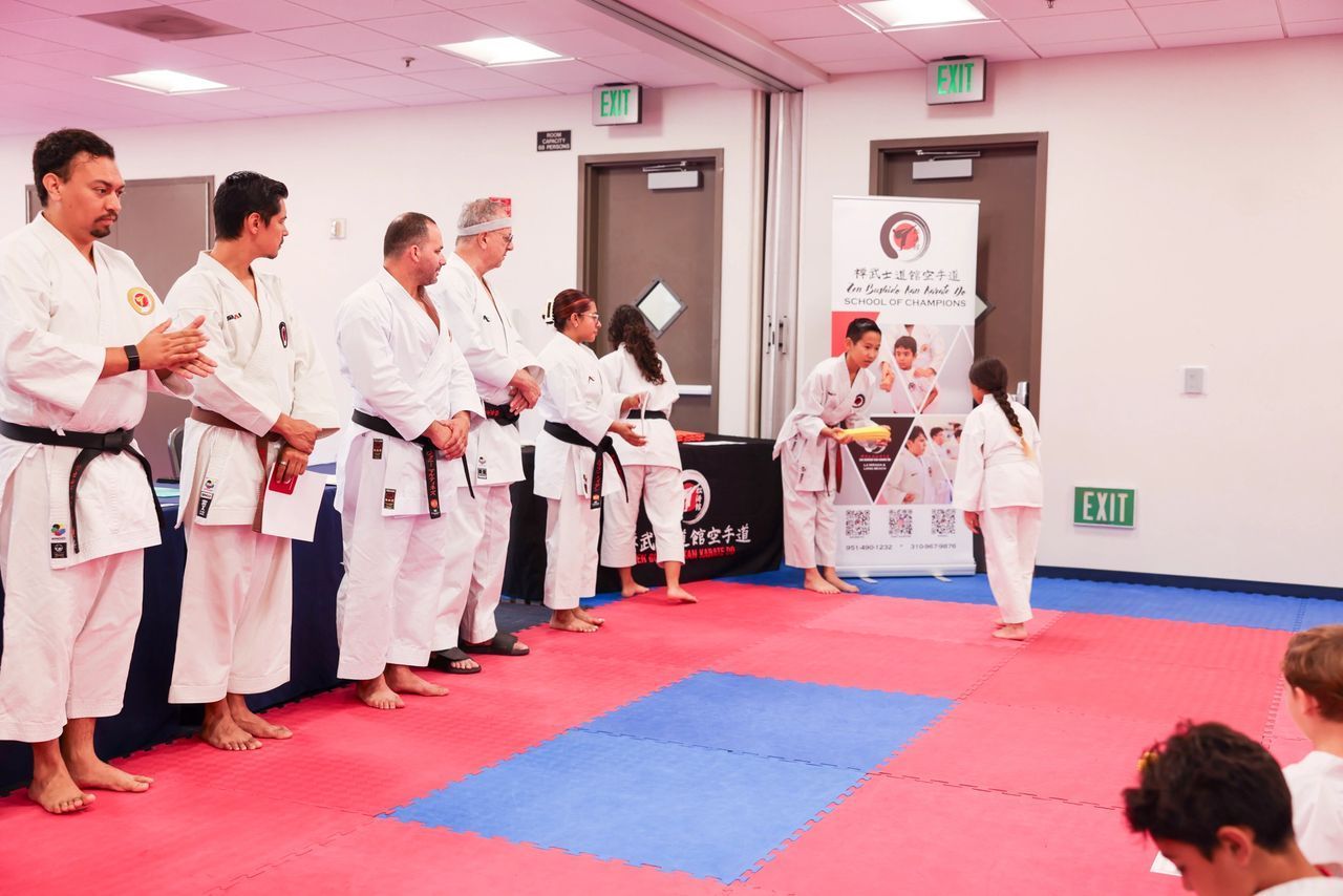 A young girl is receiving her new belt from a group of senseis