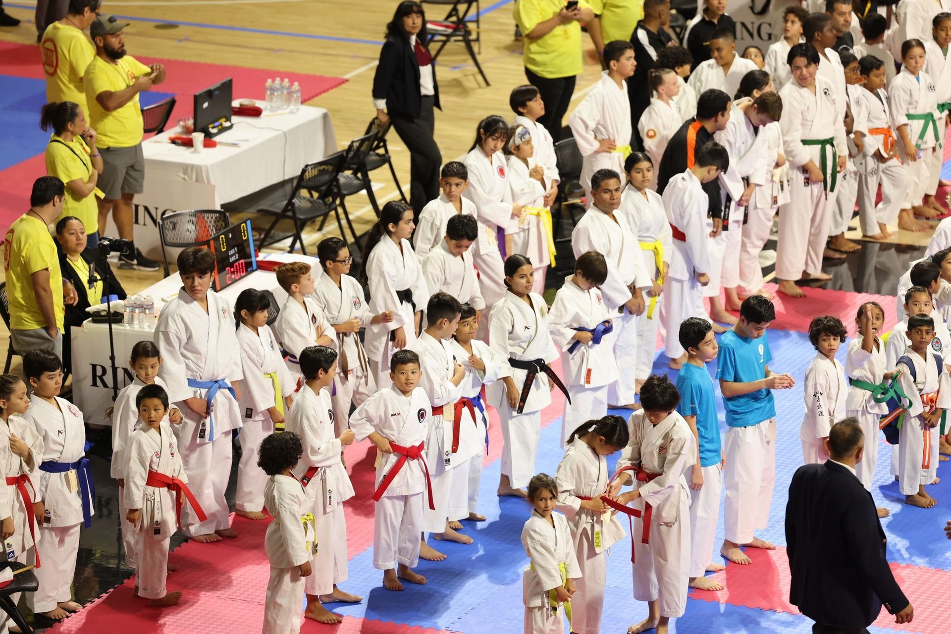 A group of children in karate uniforms are standing on a mat in a gym.