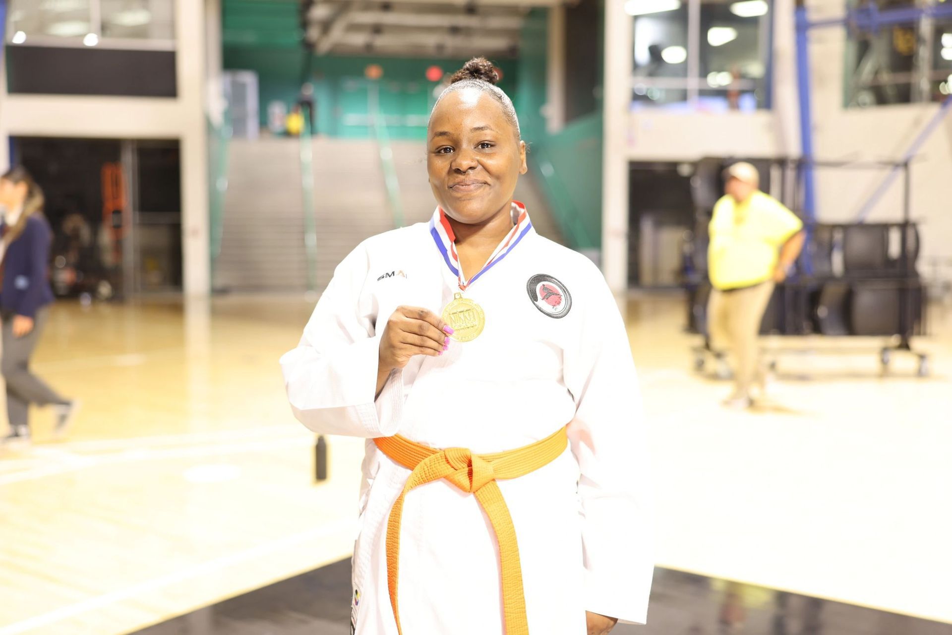 A woman in a white karate uniform is holding a gold medal.
