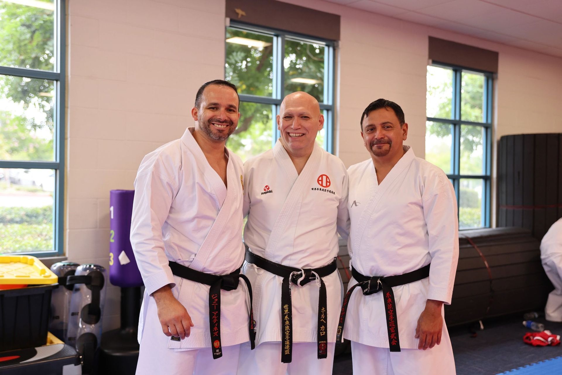 Three men in karate uniforms are posing for a picture in a gym.