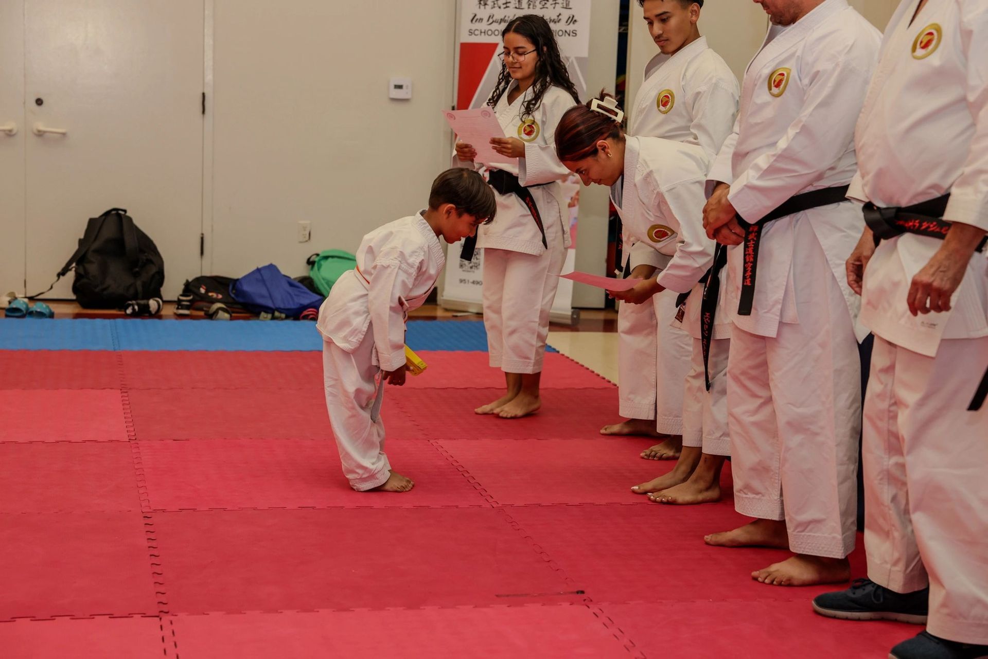 A group of people in karate uniforms are standing on a red mat.