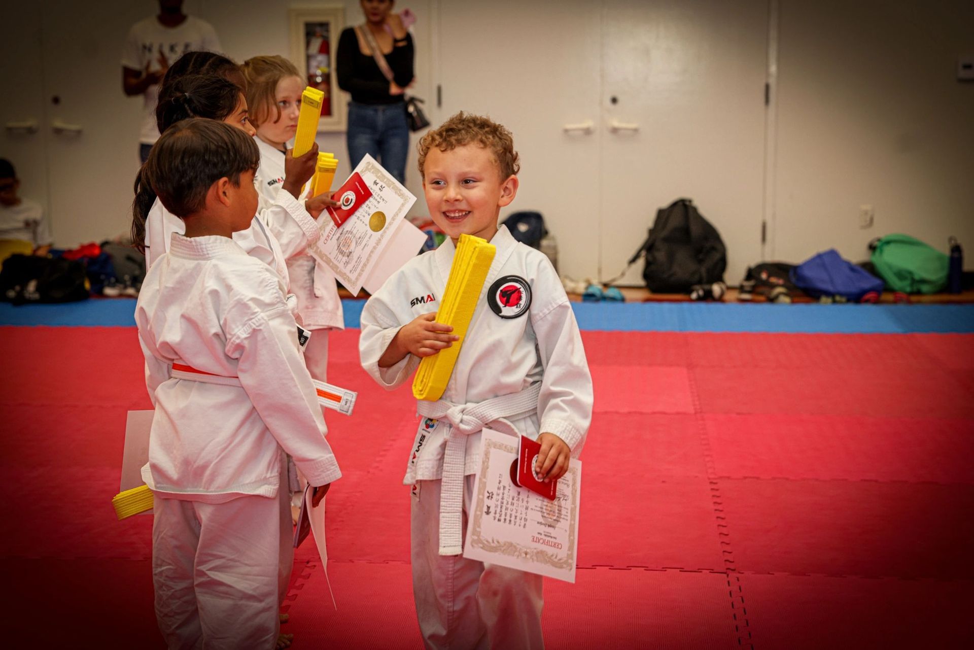 A group of young boys in karate uniforms are standing on a red mat holding certificates.