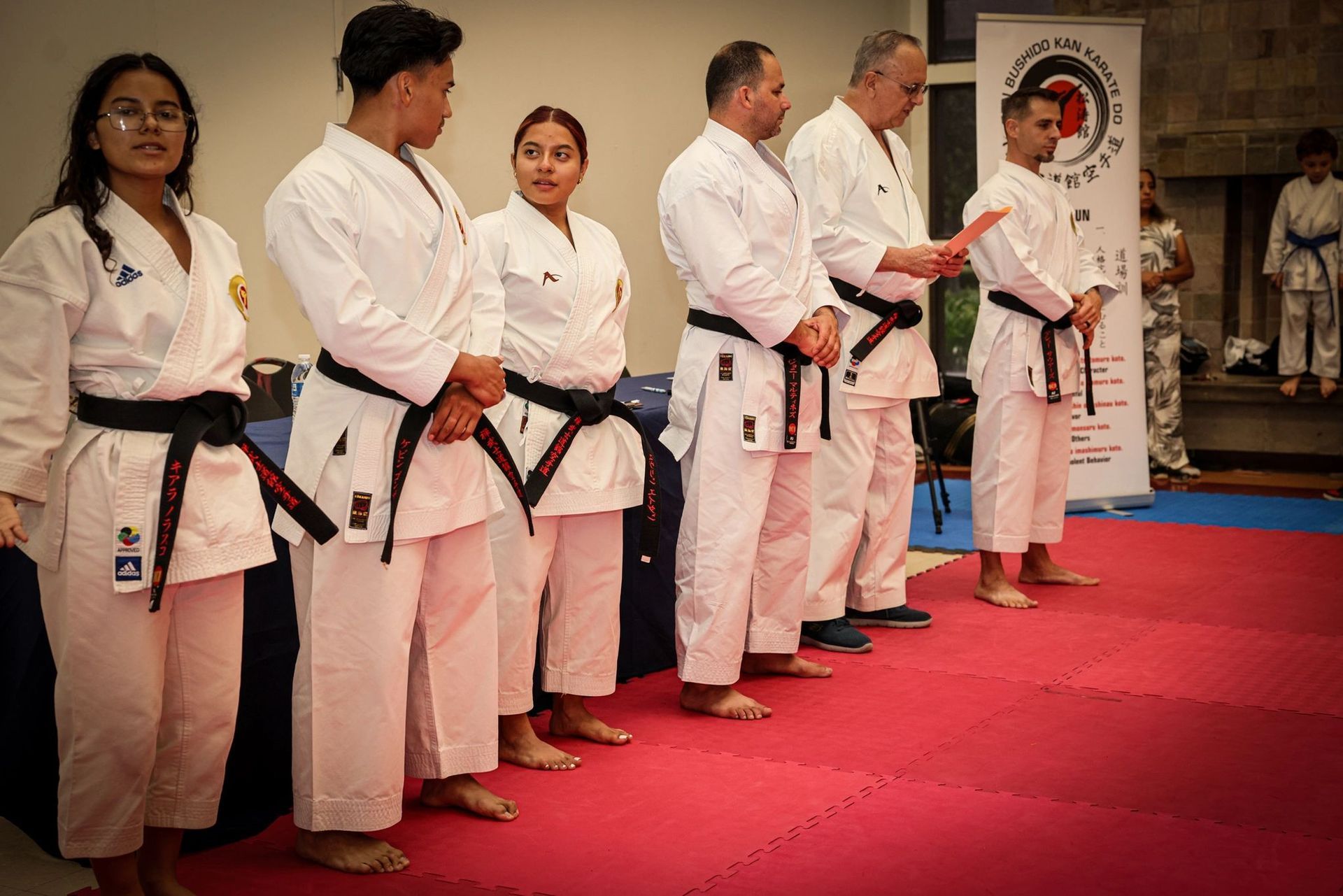 A group of people in karate uniforms are standing next to each other on a red mat.