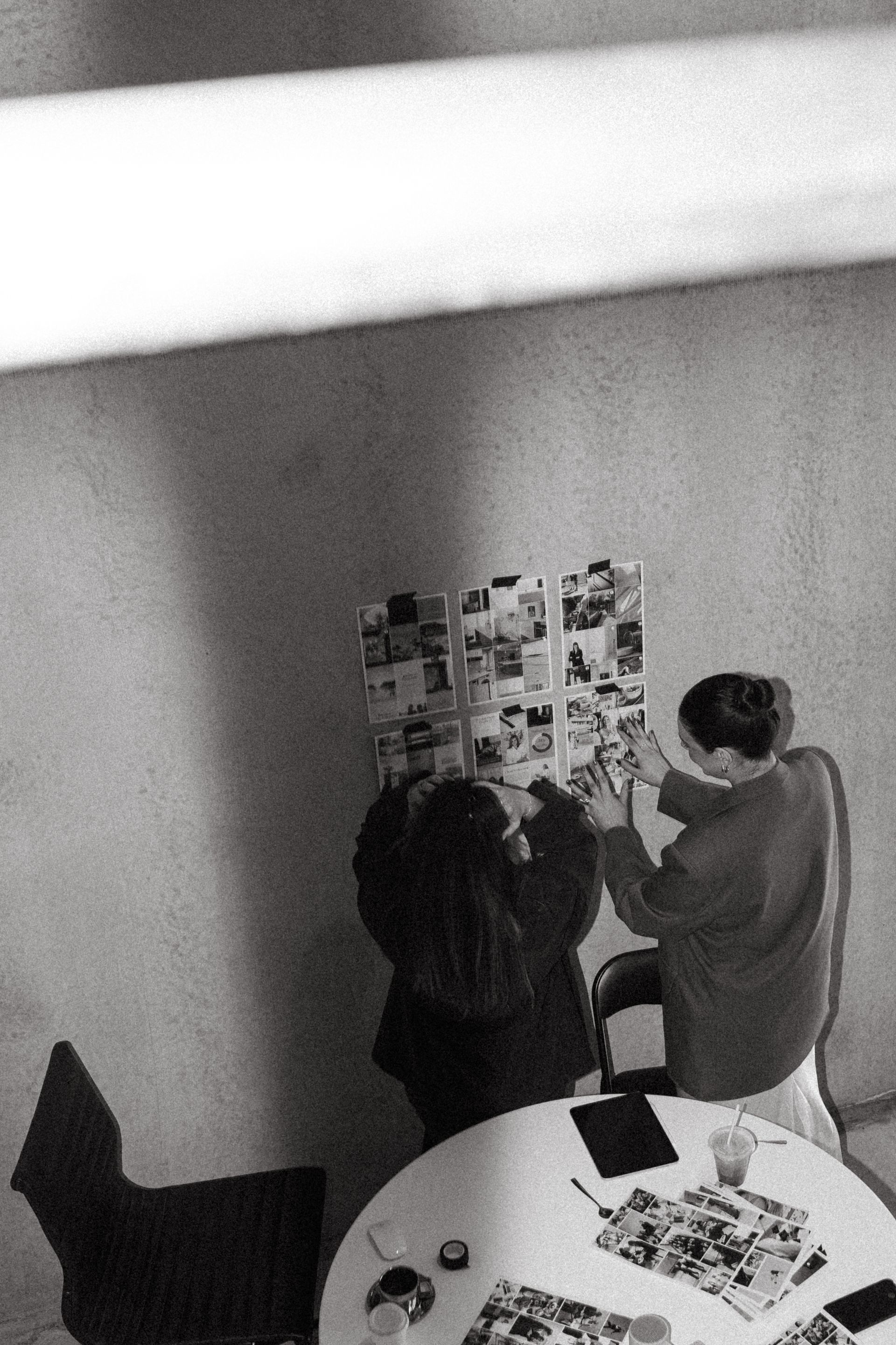 A black and white photo of two people looking at pictures on a wall.
