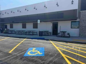 A handicapped parking spot in front of a building with picnic tables.
