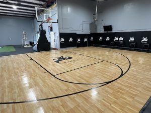 A basketball court with a wooden floor and a basketball hoop in a gym.