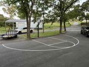 A basketball court in a driveway with a trailer parked next to it.
