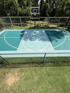 A basketball court in a backyard with a fence and trees in the background.